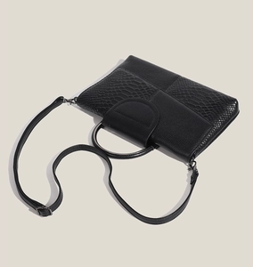 Detail view of black crocodile pattern leather bag with metal handle and shoulder strap