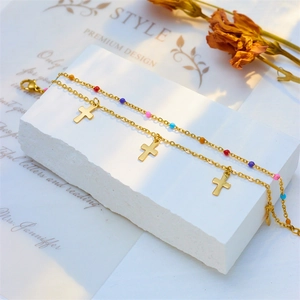 Detail of double-layer gold anklet featuring colorful beads and cross pendants on stone