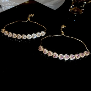 Macro view of gold heart bracelets with pink and white cubic zirconia on black surface