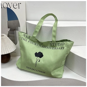Detail of light green canvas tote bag with black floral art and NKK ART STUDIO text