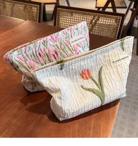 Detail of canvas tulip embroidery travel makeup bags with golden zippers on wooden table