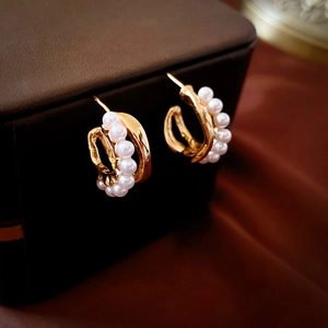 Close-up of golden double C-shaped layered pearl earrings on a luxury brown jewelry box
