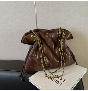 Detailed shot of brown quilted leather bag with gold chain strap on business magazine