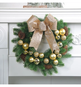 Detail of Christmas wreath with golden bow, ornaments and pine cones on a white mantel