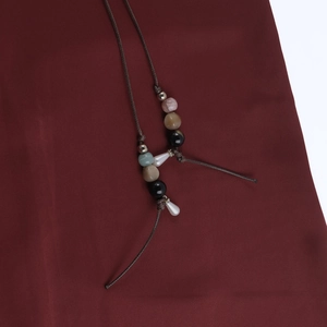 Detail of beaded necklace with mint green and pearl drops on dark red fabric background