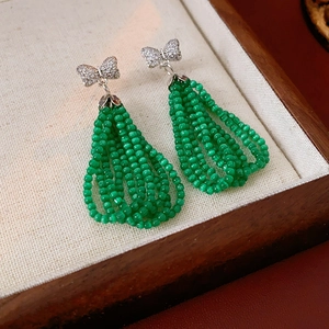 Close-up of silver bow earrings with green beaded tassels on a wooden jewelry display tray