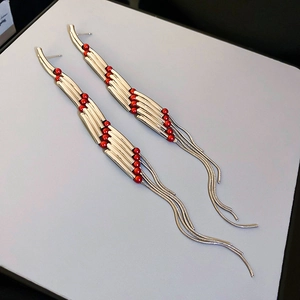 Detail of gold metal tubes and red beads with snake chain tassels on elegant earrings