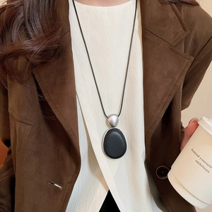 Gros plan d'un collier pendentif ovale en bois minimaliste sur une veste en daim marron avec café
