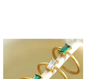 Close-up of three gold rings set with green and clear rectangular zircon stones