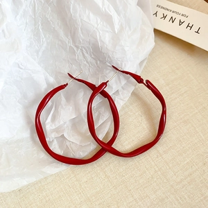 Detailed view of large red twisted hoop earrings on textured fabric and paper