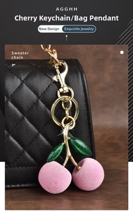 Pink flocked cherry keychain with green glitter leaves and gold hardware on a black bag