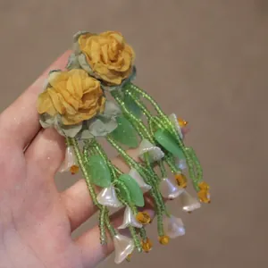 Detail of floral earrings with yellow cloth roses and green beaded tassels with leaf charms
