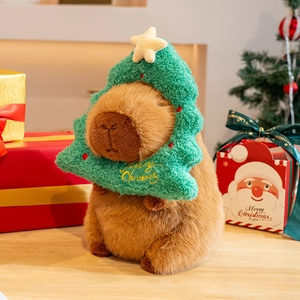 Christmas capybara plush toy in green tree costume on wooden table with holiday gift boxes