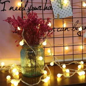 Warm yellow LED globe string lights wrapped around a glass vase for Christmas decor
