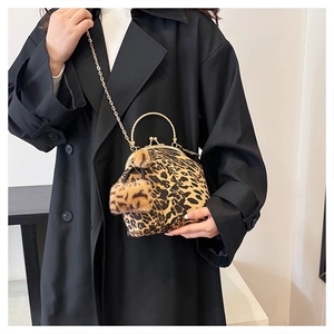 Detail of leopard print shell bag featuring gold metal handle and plush pompom charms