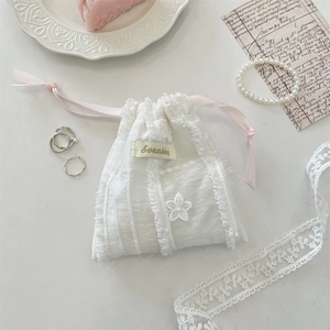 Close-up of white lace drawstring pouch with pink silk ribbon and floral appliqué detail