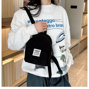 Model wearing a black corduroy mini backpack against a bookshelf, showing casual style