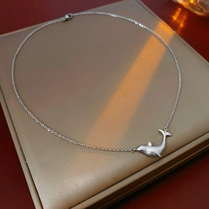 Artistic close-up of a silver whale pendant necklace on a beige display pad with warm light