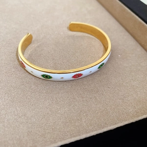 Détail d'un bracelet jonc œil maléfique doré avec émail blanc et pierres colorées