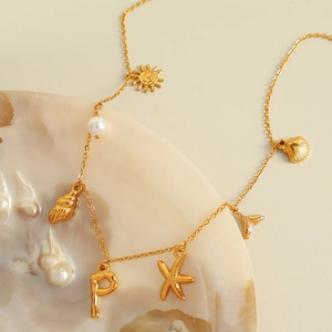 Golden necklace with ocean-themed charms like starfish and pearls on a white shell