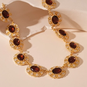 Close-up of vintage gold necklace with deep red faceted stones and white enamel detail