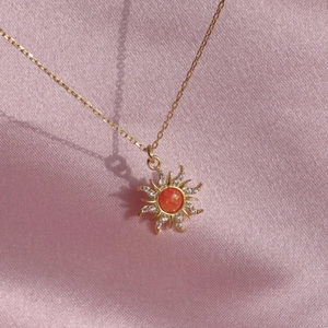 Golden sun pendant necklace with orange opal and zircon on pink silk fabric background