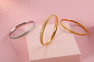 Detailed close-up of matte gold and silver bangles on elegant pink geometric props