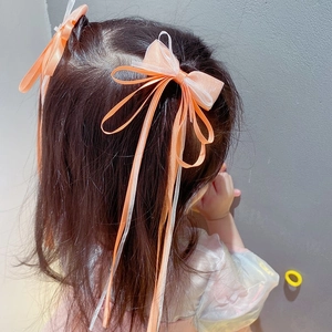 Close-up of a girl wearing two orange ribbon bow hair clips with long mesh streamers
