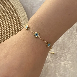 Detail of a gold stainless steel star bracelet with evil eye charms on a female wrist