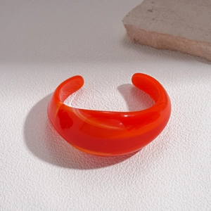 Detail of a modern bright orange acrylic bangle with marble texture and open cuff design