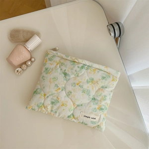 Detail of floral quilted cosmetic bag with zipper and logo tag on a minimalist desk