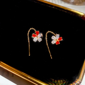 Detailed close-up of gold-plated flower drop earrings with red enamel and white zircon on velvet
