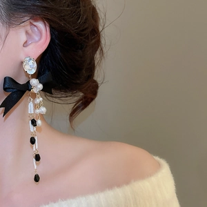 Close-up of elegant bow pearl tassel earrings worn by a model in soft studio lighting