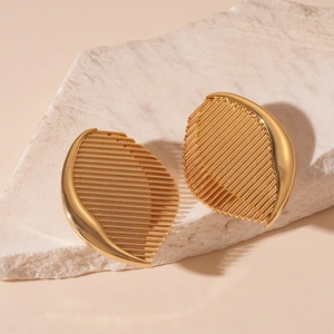 Detail of golden semi-oval earrings with linear texture on a white stone background