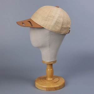 Side view of beige raffia baseball cap with hollowed-out brown leather brim on mannequin