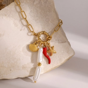 Dettaglio di collana nautica dorata con stella marina, peperoncino e perle su una pietra