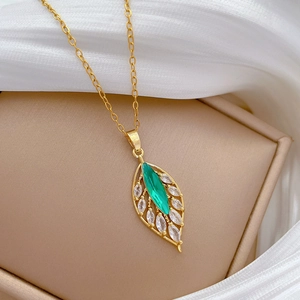 Close-up of golden leaf necklace pendant with green gemstone and small clear crystals