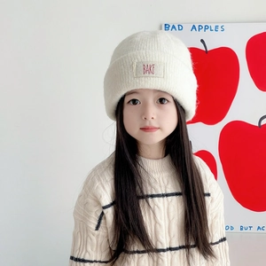 Detail of white knit winter hat with BAKE cloth label worn by a child on white background