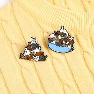Enamel lapel pins featuring stacked cartoon cats and tea cup kittens on yellow knitwear