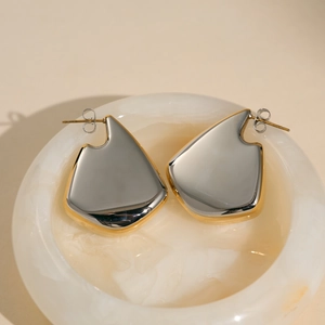 Polished silver and gold tone fan shaped steel earrings on marble surface