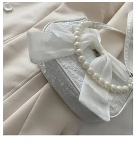 Detail of elegant white handbag with large satin bow and premium pearl handle