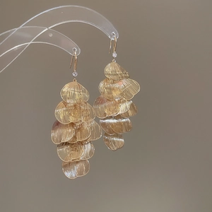 Detail of gold petal tassel earrings with brushed texture and small crystal on ear hook