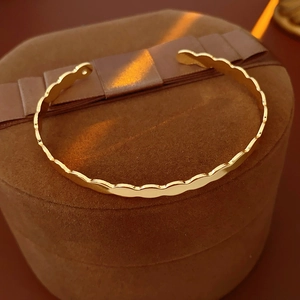 Close-up of golden wavy cuff bracelet on a premium velvet jewelry box with warm lighting