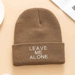 Close-up of LEAVE ME ALONE white embroidery on brown ribbed knit beanie hat