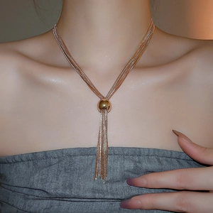 Dettaglio collana a strati con nappe dorate e cursore a sfera su una modella