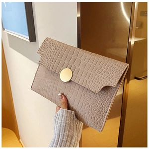 Detail of light brown crocodile texture envelope bag with golden round buckle in hand