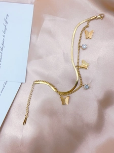 Detail eines goldfarbenen Edelstahlarmbandes mit Schmetterlingsanhängern und Kristallen