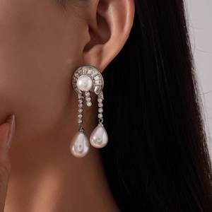 Close-up of geometric drop earrings with white pearls and sparkling zircon accents