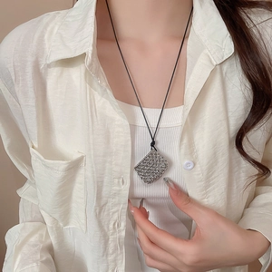 Close-up of a silver hollow square mesh pendant on a black cord necklace worn by a model