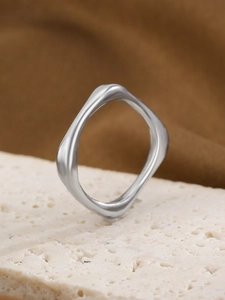 Close-up of wavy geometric silver stainless steel ring on a textured stone pedestal